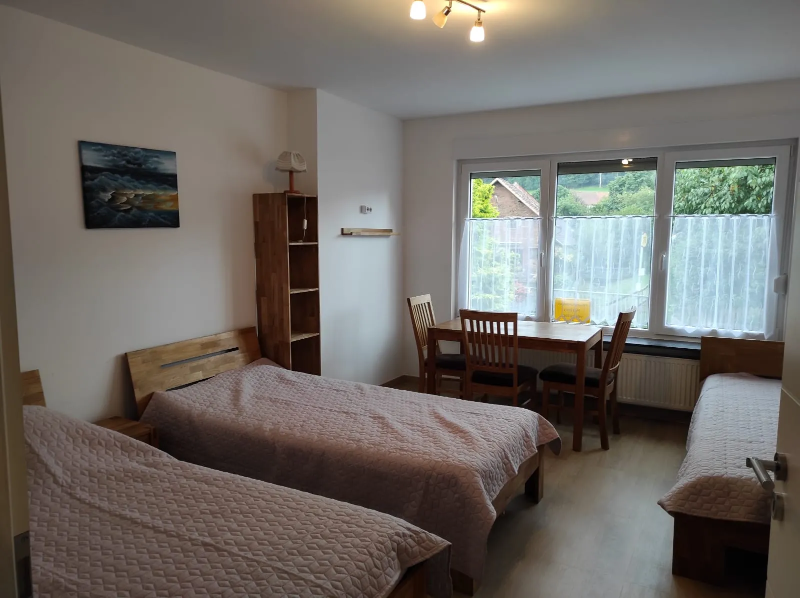 Schlafzimmer mit drei Betten und Esstisch am großen Fenster